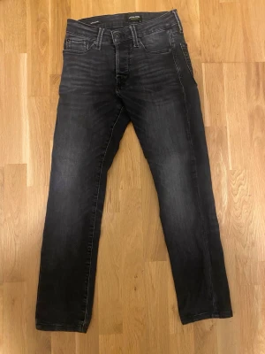 Svarta jeans från Jack & Jones - Snygga svarta jeans från Jack & Jones med diskret tvättad look. Klassisk femficksmodell med raka ben och normal midja. Perfekta till en avslappnad stil och passar till det mesta. Materialet är mjukt och stretchigt för extra komfort.