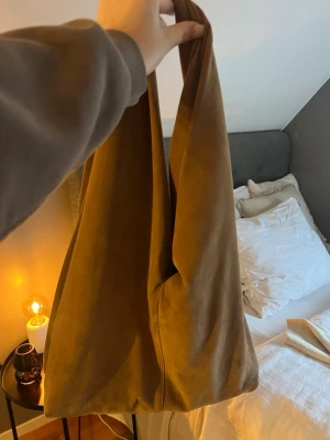 Beige mockaväska - En enkel och stilren beige väska i mjukt tyg. Väskan har en slouchy form med långa handtag som gör den lätt att bära över axeln. Perfekt för att slänga ner allt du behöver när du är på språng.