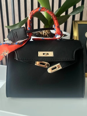 Svart handväska med gulddetaljer - . Tillverkad i läder med strukturerad finish och elegant form.