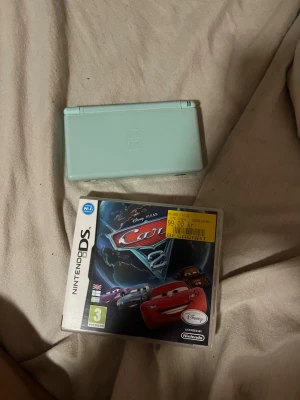 light blue Nintendo DS lite with Pixar Cars 2 - game - Selling a light blue Nintendo DS Lite with the classic foldable design and two screens. Comes with the game Cars 2 from Disney Pixar. Perfect for anyone who enjoys portable gaming and retro gaming.