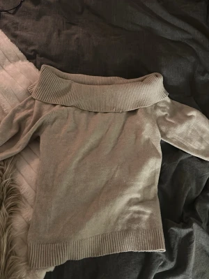Beige stickad ofshoulder tröja Gina Tricot - Säljer en beige stickad tröja från Gina Tricot med bred polokrage och ribbade muddar. Tröjan har en avslappnad passform och är perfekt för kyligare dagar. Materialet är mjukt och bekvämt, vilket gör den enkel att styla till olika outfits.