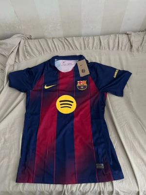 Barcelona matchtröja Nike blå/röd - Säljer en officiell FC Barcelona matchtröja från Nike i blått och rött med gula detaljer. Tröjan har klubbmärke, Nike-logga och Spotify som sponsor på bröstet. Tillverkad i lätt och ventilerande material, perfekt för fotboll eller träning.