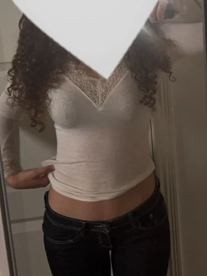 Intimissmi  - Säljer en vit långärmad topp med v-ringning och fina spetsdetaljer vid halsringningen och ärmsluten. Toppen har en slim passform och är tillverkad i ett mjukt material som sitter skönt mot kroppen. Perfekt att styla med jeans eller kjol.