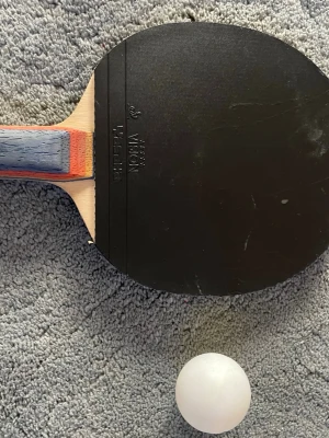 Pingisracket och boll Stiga Vision - Säljer ett pingisracket från Stiga Vision med svart och röd gummiyta samt ett blått, rött och träfärgat handtag. Medföljer en vit pingisboll. Perfekt för dig som vill spela bordtennis med kompisar.