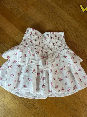 Blommig kjol - Supersöt kort kjol i vit bomull med rosa blommigt mönster! Aldrig använd, men bortklippa lappar. Köpt i Spanien (tror Urban outfitters)
