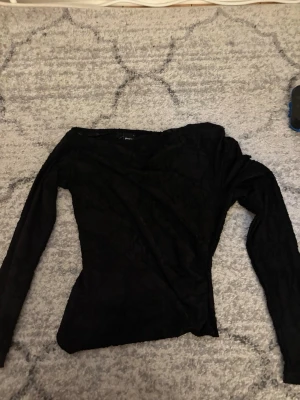 Svart omlottopp från Gina Tricot - Snygg svart omlottopp från Gina Tricot med lång ärm och figurnära passform. Ena ärmen är Off-shoulder💕