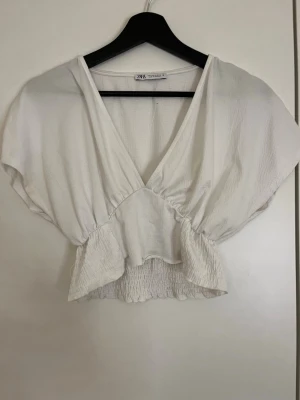 Vit croppad omlottopp från Zara - Säljer en vit croppad omlottopp från Zara med v-ringning och korta ärmar i bra skick 
