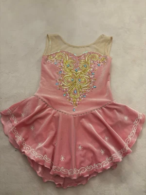 Rosa glittrig kortklänning med paljetter - Rosa konståknings klänning med glittriga paljetter och broderier i guld, blått och vitt. Klänningen har mesh upptill, är ärmlös och har dubbla kjollager med vita broderade detaljer längs kanten. Materialet är glansigt och stretchigt, perfekt för en unik look på isen🧊⛸️ vid frågor, kontakta mig vid frågor💕 kan även minska priset💕⛸️