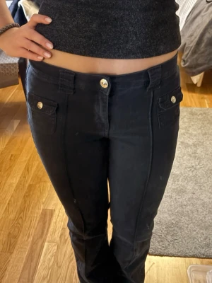 Svarta jeans med fickdetaljer - Säljer ett par svarta jean med snygga framfickor. Jeansen har bred linning och bälteshällor, vilket ger en cool och modern look. Perfekta till en avslappnad outfit och passar till det mesta. Byxorna har sprättats upp längst ner för att bli lite längre (se sista bilden)🤗