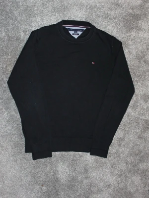 Svart tröja från Tommy Hilfiger - Klassisk svart tröja från Tommy Hilfiger med rund halsringning och diskret logga på bröstet. Tröjan har långa ärmar och ribbade muddar vid ärmslut och nederkant. Perfekt till jeans för en clean och stilren look modellen är 181 och bär vanligtvis S/M.🌟 hör gärna av dig med frågor🌟