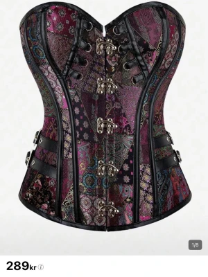 Mönstrad korsett med metallspännen - Säljer en färgstark korsett med patchwork-mönster i lila, turkos och svart. Korsetten har dekorativa metallspännen framtill, svarta detaljer och justerbara band i sidan. Materialet är glansigt tyg med inslag av brokad och konstläder. Perfekt för dig som vill sticka ut! Varan har aldrig blivit använd🤍