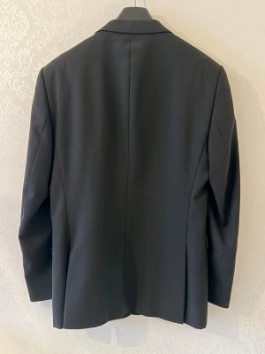 Svart kavaj från dressmann - Klassisk svart kavaj från dressmann med smal passform och enkelknäppning. Perfekt för en dressad look och funkar till många olika outfits. Använd 3 gånger bara 