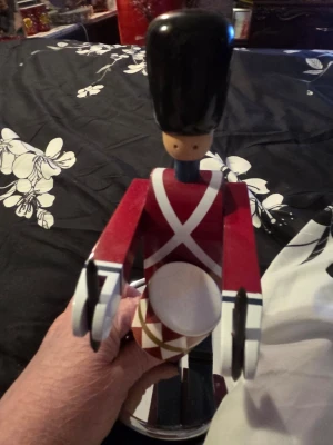 Kay Bojesen Träfigur trumslagare soldat - Säljer en dekorativ träfigur föreställande en trumslagare soldat med röd uniform, vita detaljer och svart hög hatt. Figuren har vita armar och håller en trumma med röd-vitt mönster. Perfekt som prydnad eller samlarobjekt.