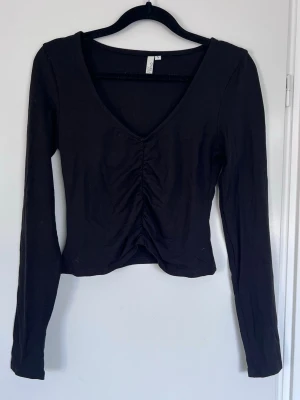 Svart långärmad topp med v-ringning, storlek S - Svart långärmad topp från Nelly med snygg v-ringning och rouched-detalj fram. Clean och trendig. Perfekt nu till vår/sommar med ett par jeans eller kjol 🌸