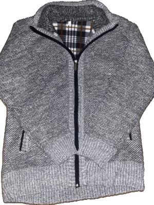 Grå stickad ziptröja med rutigt foder - Snygg grå stickad tröja med dragkedja och hög krage. Insidan har ett rutigt foder i vitt, svart och brunt. Tröjan har två fickor framtill med svarta detaljer och ribbstickade muddar vid ärmslut och nederkant. Perfekt för kyliga dagar.