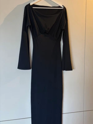Svart långärmad långklänning - En stilren svart långklänning med långa ärmar och bred, något offshoulder ringning. Klänningen har en figurnära passform och är tillverkad i ett mjukt, stretchigt material som ger en snygg siluett. Perfekt för dig som gillar minimalistisk och elegant stil. Går nästan ner till marken på mig som är 170cm, perfekt om man vill sätta till en klack. Enbart använd en gång. XS men mer som S. 
