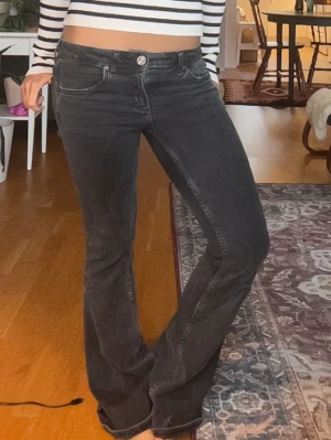 Svarta bootcut jeans med hög midja - Säljer ett par svarta bootcut jeans med hög midja och klassiska fem fickor. Jeansen har en snygg tvättad look och stängs med knapp och dragkedja. Perfekta för dig som gillar en avslappnad men trendig stil.