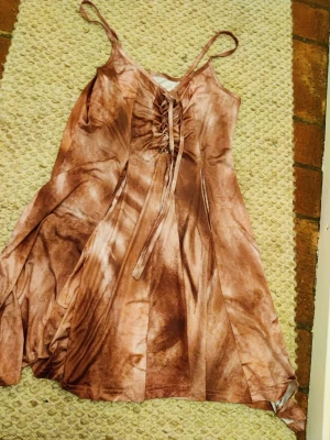 Brun omlottklänning med snörning tie dye hippie  - En fin Peach klänning med tunna axelband och snygg snörning framtill. Perfekt för dig som gillar boho-vibbar och vill sticka ut lite extra.