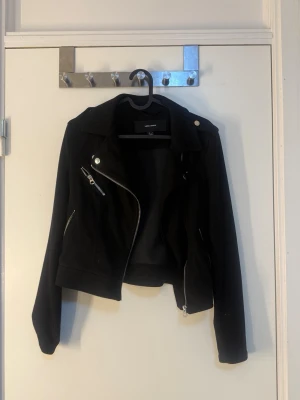 Svart skinnjacka från vero Moda  - Cool svart skinnjacka från Cubus med asymmetrisk dragkedja, silverfärgade detaljer och klassisk krage. Jackan har två fickor med dragkedja och snygga axelknappar. Perfekt för dig som vill ha en edgy look.