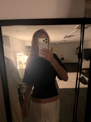 Svart croppad topp med knyt i ryggen - Snygg svart croppad topp med korta ärmar och öppen rygg med knytband. Perfekt för dig som vill ha en trendig och stilren look. Toppen har en tight passform och är tillverkad i ett mjukt material som känns skönt mot huden.