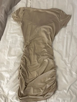 Beige omlottklänning med snörning - Trendig beige kortklänning med omlottdetalj och snörning i midjan. Klänningen har korta ärmar och är tillverkad i ett mjukt, stretchigt material som ger en snygg passform. Perfekt för dig som gillar stilrena och moderna plagg.