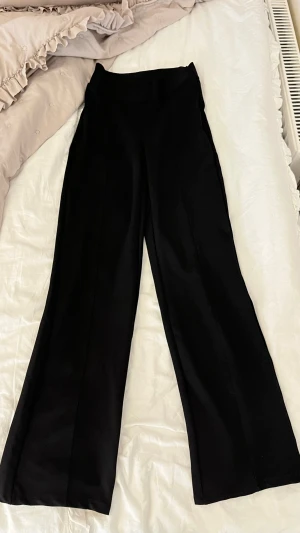 Svarta vida kostymbyxor - Säljer ett par svarta kostymbyxor med hög midja och vida ben. Byxorna har pressveck framtill för en clean look och är tillverkade i ett mjukt, vävt material. Perfekta för dig som gillar en stilren och trendig outfit.