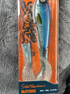 Svartzonker McHybrid fiskedrag - Säljer ett oöppnat Svartzonker McHybrid fiskedrag, 20 cm långt och väger 100 g. Draget har blå och silverfärgad kropp med glitterdetaljer och mjuk paddel. Tillverkat av slagtålig ABS-plast och miljövänlig zink. Perfekt för sportfiske och predatorfiske.