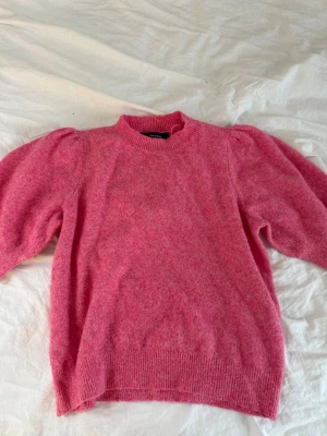 Rosa puffärm stickad tröja - Säljer en stickad tröja i härlig rosa färg med puffärmar och rund hals. Tröjan har ribbade muddar vid ärmslut och nederkant, vilket ger en snygg och trendig look. Perfekt för dig som vill ha något mjukt och bekvämt i garderoben.