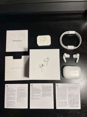 Apple AirPods Pro trådlösa hörlurar - Säljer ett par vita Apple AirPods Pro med laddningsetui, originalkartong, USB-C laddkabel och extra öronproppar. Hörlurarna har en stilren och kompakt design i blank plast och levereras med all originaldokumentation. Perfekta för musik, samtal och träning.
