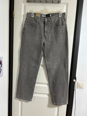 Grå raka jeans från Levi's - Säljer ett par grå jeans från Levi's med rak passform och klassisk femficksdesign. Jeansen har normal midja, bälteshällor och dragkedjegylf. Tillverkade i slitstark denim som passar perfekt till en avslappnad stil.