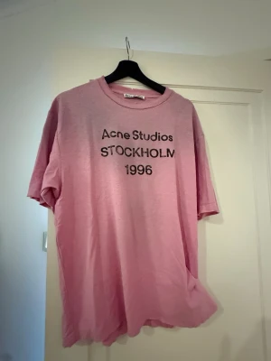 Rosa Acne Studios t-shirt - Säljer en rosa t-shirt från Acne Studios med trycket 'STOCKHOLM 1996' på bröstet. Klassisk rund hals och korta ärmar. Skön och avslappnad passform, perfekt till jeans eller shorts. Materialet känns mjukt och är troligtvis bomull.