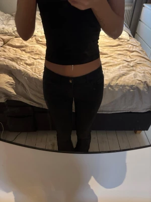Svarta bootcut jeans med låg midja - Säljer ett par svarta skinny jeans med hög midja och klassisk femficksdesign. Jeansen har smal passform och stängs med knapp och dragkedja. Perfekta till crop tops och sneakers för en clean look. Tyvärr har de lossnat färg på knappen!