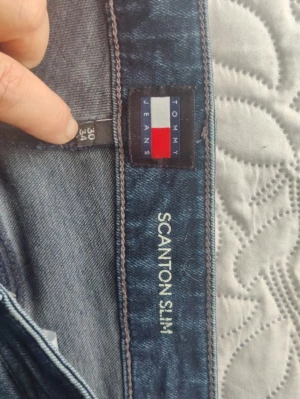 Tommy Jeans Scanton Slim blå jeans - Säljer ett par blå slim fit jeans från Tommy Jeans, modell Scanton Slim. Jeansen har klassisk femficksdesign, normalhög midja och subtila slitningar framtill för en avslappnad look. Perfekta till vardagsstilen och tillverkade i mjukt denimtyg.