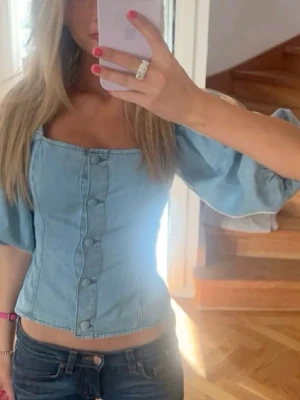 Ljusblå denimtopp - Trendig ljusblå topp i denim med puffiga korta ärmar och snygga knappar framtill. Toppen är använd fåtal gånger och är i superbra skick, så fin till sommaren. 🩷🩷🩷