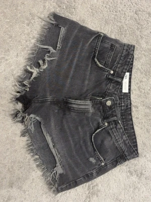 Svarta jeansshorts från Zara - Säljer ett par svarta jeansshorts från Zara med råa, fransiga kanter och slitningar.Shortsen har fem fickor, knapp och dragkedja framtill, mid waist . Storlek 40 men som S