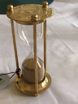 Timglas i glas och guldmetall - Snyggt timglas med glasbehållare och guldfärgad metallram. Toppen har ett detaljerat blommönster och sanden inuti är ljusbrun. Perfekt som dekoration eller för att hålla koll på tiden på ett stilfullt sätt. Ca 5 min