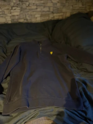 Mörkblå halvzip från Lyle & Scott - Mörkblå sweatshirt med halv dragkedja från Lyle & Scott Junior. Tröjan har ett gult logomärke på bröstet och är tillverkad i mjukt bomullsmaterial. Perfekt för en avslappnad och stilren look.
