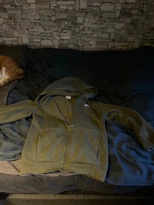 Olivgrön zip hoodie från Nike - Säljer en olivgrön hoodie från Nike med dragkedja framtill och klassisk huva. Hoodien har två fickor på magen och är tillverkad i mjukt material som känns skönt mot huden. Perfekt för chill dagar eller när du vill ha en sportig look.