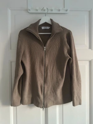 Beige ziptröja från Ljung by Marcus Larsson - Snygg beige ribbad tröja från Ljung by Marcus Larsson med dragkedja framtill och hög krage. Tröjan har långa ärmar och är tillverkad i ett mjukt, stretchigt material.  Enkel att matcha med olika outfits.