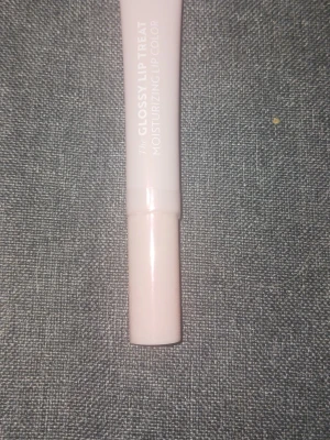 Glossy Lip Treat läppglans rosa - Säljer ett Glossy Lip Treat läppglans i en ljusrosa tub. Läppglanset ger en glansig finish och har en återfuktande formula. Förpackningen är smidig och enkel att ta med i väskan. Perfekt för dig som vill ha mjuka och glansiga läppar. Plasten är kvar