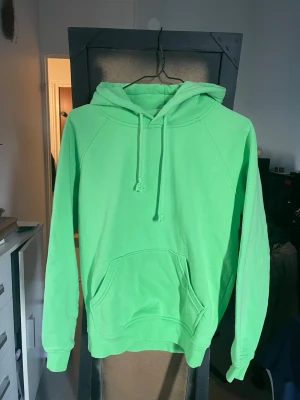 Grön hoodie från Bik Bok - Snygg limegrön hoodie från Bik Bok i storlek XS. Hoodien har en klassisk känguruficka framtill, dragsko i huvan och ribbade muddar vid ärmar och nederkant. Perfekt för en chill och avslappnad stil.