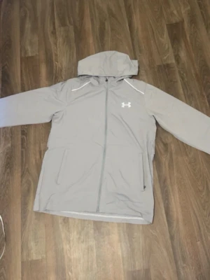 grå under armour vindjacka - lätt, bekväm och perfekt för både träning och vardag. Skyddar mot vind och passar bra till en sportig stil. Bra skick. Pris kan diskuteras vid snabb affär.