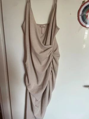 Beige klänning H&M - Trendig beige klänning från H&M fin design och smala axelband. Kläningen sitter tajt mot kroppen och sitter super snyggt på,Perfekt för dig som gillar stilrena och moderna plagg.