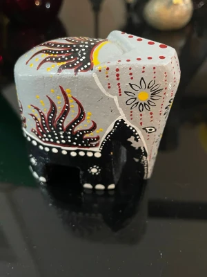  elefant i trä, handmålad - Unik handmålad elefant i trä med grå, svart, röd, gul och vit färg. Elefanten har detaljerade mönster med prickar, blommor och eldliknande former på sidorna.  Perfekt som prydnad eller samlarobjekt för digafrikanskt hantverk, ofta från Kenya, Tanzania eller Sydafrika. Sådana små träelefanter såldes mycket till turister från 1970–1990-talet. som gillar färgstarka detaljer.