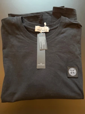 Svart Stone Island t-shirt *OANVÄND!* - NY & OANVÄND! Prislappen sitter till och med kvar! Snygg svart ”Stone Island” t-shirt med klassisk logopatch på bröstet. OBS! Märkt med storlek XL MEN den är som en LARGE!