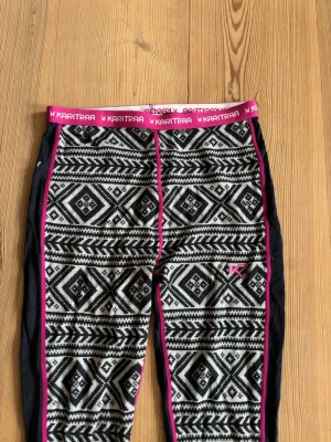 Kari Traa mönstrade ullleggings - Snygga ullleggings från Kari Traa med svartvitt nordiskt mönster och rosa detaljer. Midjeresår med logga och kontrastsömmar i rosa. Perfekta som underställ eller till träning under kalla dagar. Materialet är mjukt och stretchigt för bästa komfort.