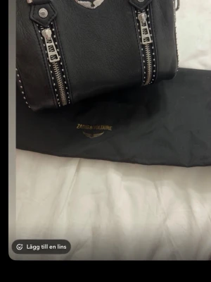 Svart handväska från Zadig & Voltaire - Snygg svart handväska i äkta läder från Zadig & Voltaire. Väskan har silverfärgade dragkedjor. Viktigt! (Missfärgningar längst upp vid dragkedjan) ( blixtlåset e krångligt) annars kmr med dustbag, modellen är sunny handväska. Nypris 5600kr