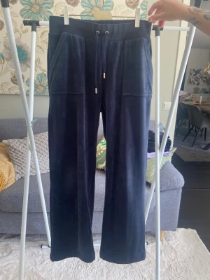 Mörkblå velourbyxor Juicy Couture - Mörkblå mjukisbyxor från Juicy Couture i mjuk velour. Byxorna har raka ben, bred resår i midjan med dragsko och stora fickor fram samt bakfickor med knapp. Dem är i bra skick men använda. 