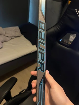 Bauer hockeyklubba med blå detaljer - Säljer en hockeyklubba från Bauer med snygga blå och svarta detaljer. Klubban har en modern design och är tillverkad i kompositmaterial, vilket gör den lätt och smidig att använda på isen.