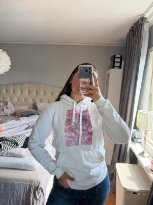 Vit hoodie med rosa tryck - Snygg vit hoodie från The Cool Elephant med huva och dragsnören. På bröstet finns ett stort rosa och lila grafiskt tryck🩷💜🤍 på ryggen finns en liten fläck som knappt syns (se sista bilden!)